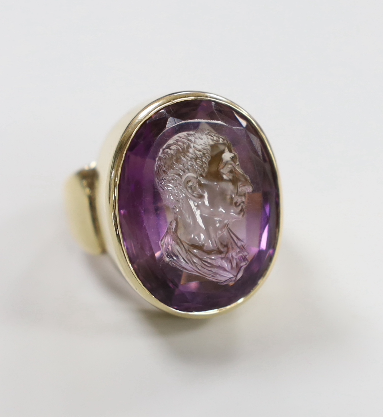 A modern 9ct yellow gold and amethyst intaglio set oval ring, carved with the head of a gentleman to sinister, size O, gross weight 18.2 grams.